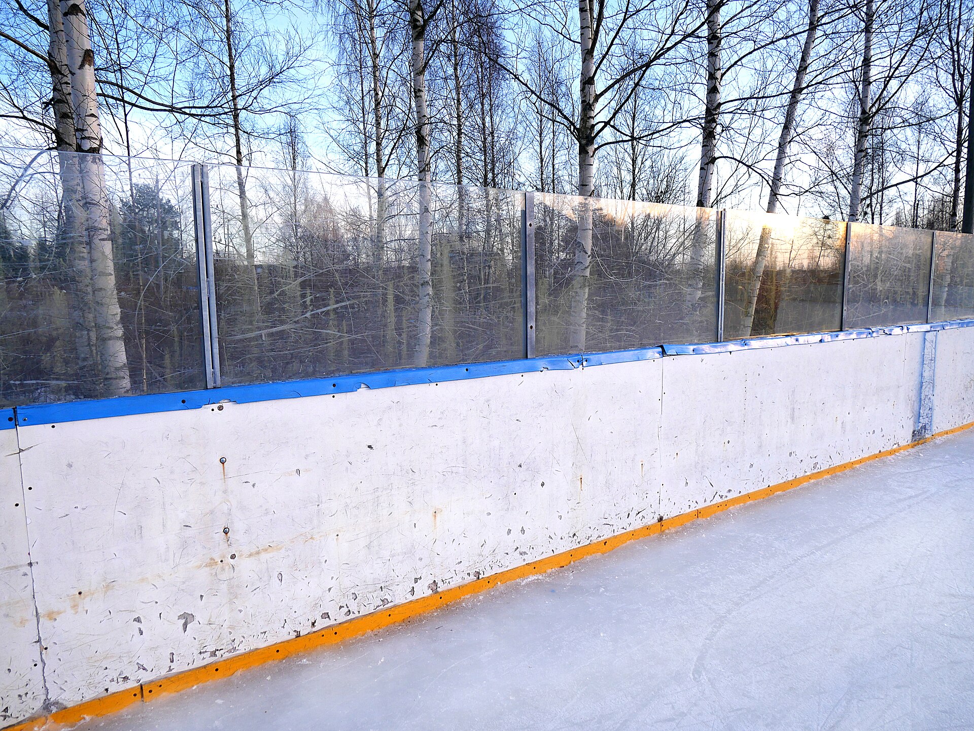 The boards of an outdoor rink with bare winter trees behind them